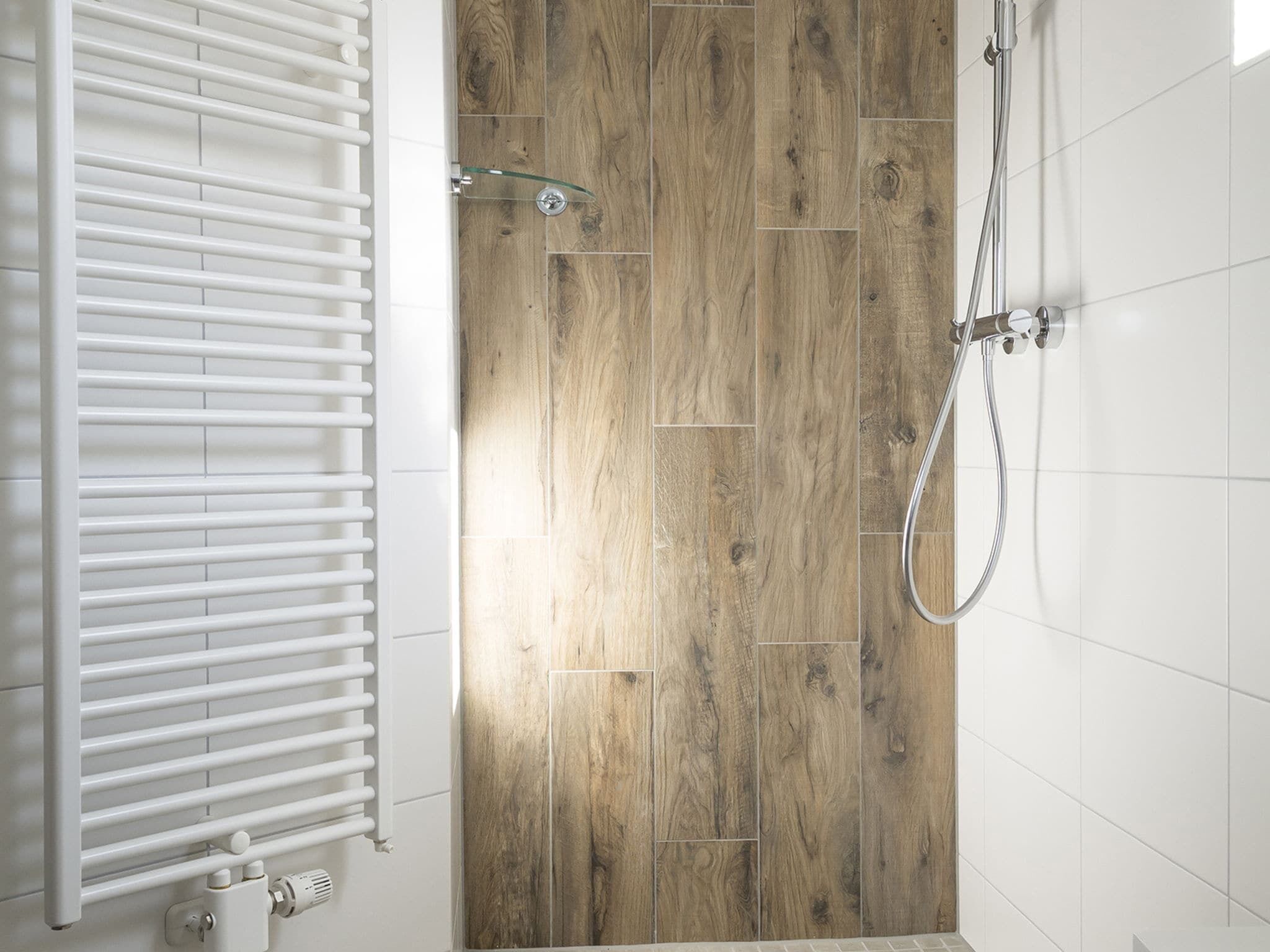 Un baño con puerta de madera, ducha y radiador blanco.