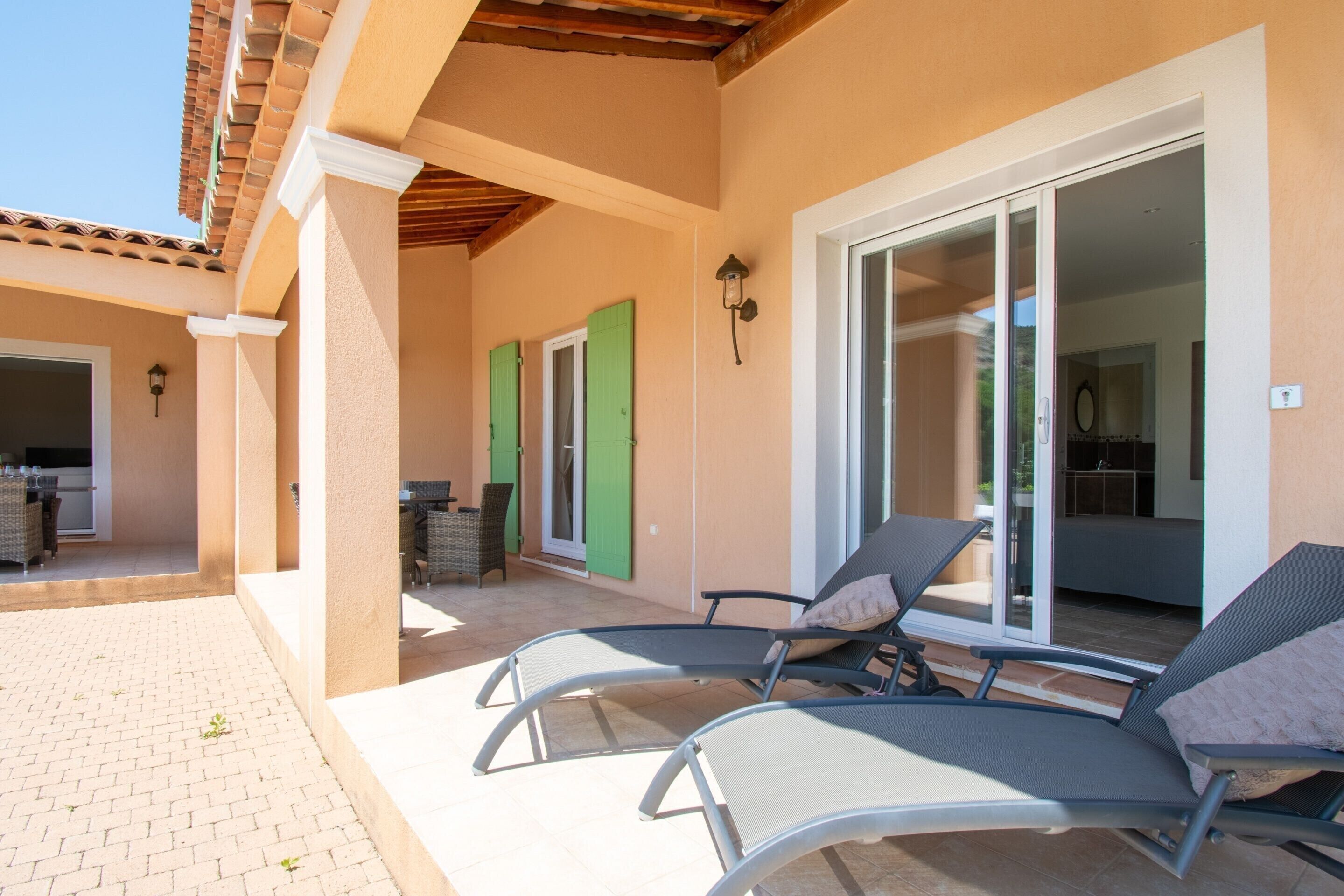 Un espacio al aire libre techado con sillones de descanso, una mesa de patio y una puerta corrediza de vidrio que da a una habitación.