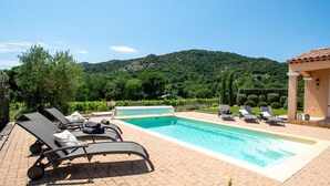 Ein Swimmingpool mit Liegestühlen, einer Pergola und Blick auf einen grünen Hügel.