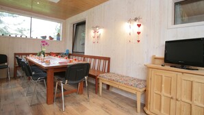 Ein Essbereich mit einem Holztisch, Stühlen und einer Bank. Ein Fernseher steht auf einer Holzkommode.