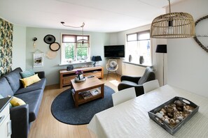 A living room with a sofa, coffee table, TV, and a dining table with a tray of snacks. - Apartment in Callantsoog Near North Holland Coast (t Zand)