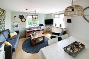A living room with a sofa, coffee table, TV, and a dining table with a tray of snacks.