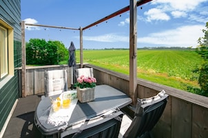 A wooden deck with a table and chairs, overlooking a green field.