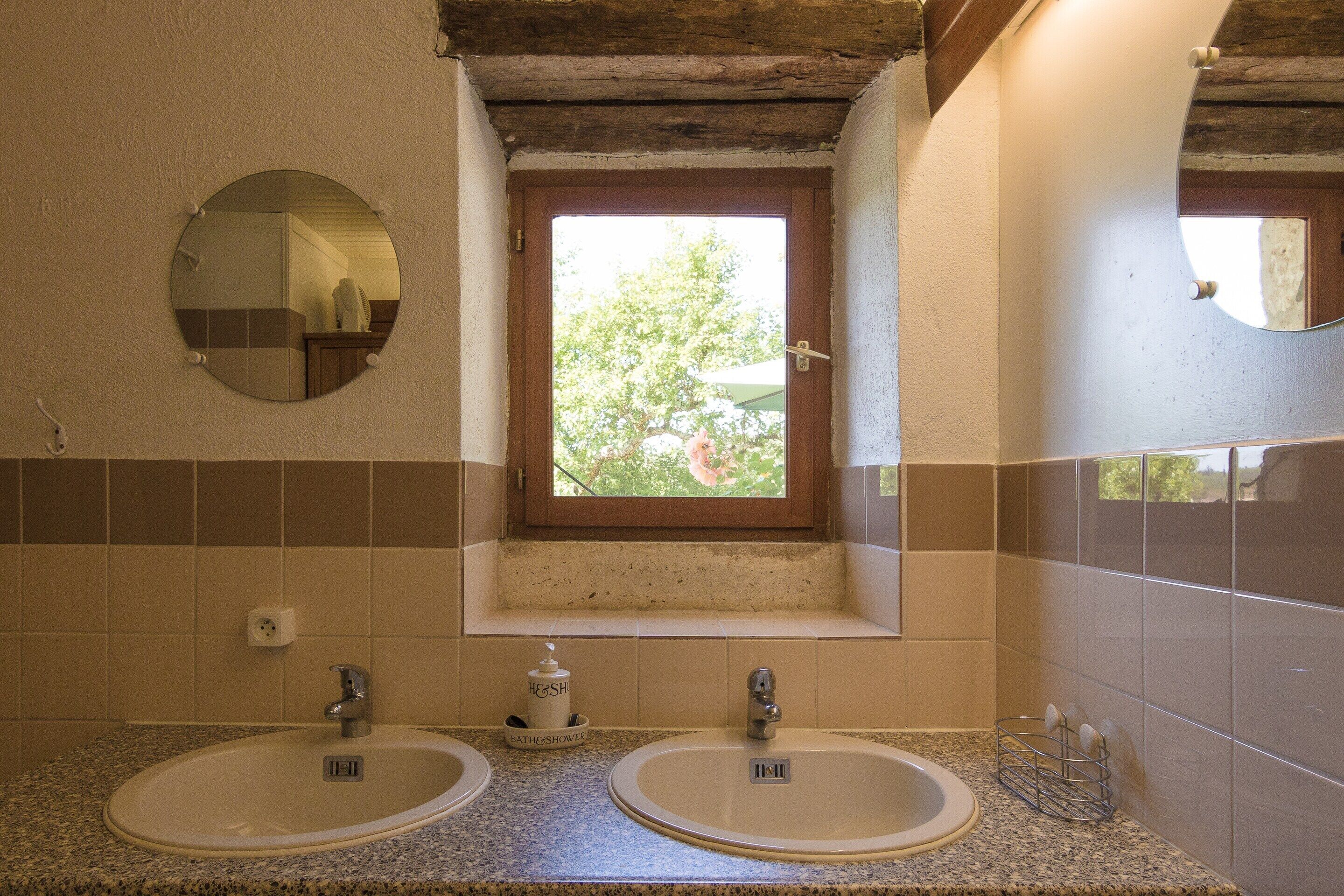A bathroom with two sinks, a window, and a mirror.
