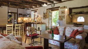A rustic kitchen with wooden beams, a dining area with chairs and a table, and a cozy living room with a sofa and cushions. - Holiday Home in Dordogne With Private Pool (Thenon)
