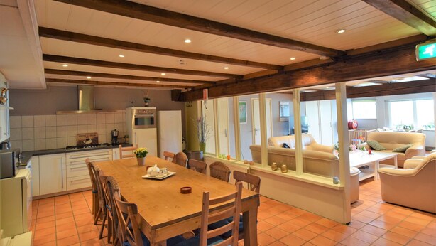 A spacious kitchen with wooden beams, a dining area with a wooden table and chairs, and a living area with a sofa and armchairs. - Quaint Farmhouse near River in Oosterwijk (Oosterwijk)