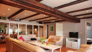 A spacious living area with a high ceiling, a television on a white cabinet, and a dining area in the background. - Quaint Farmhouse near River in Oosterwijk (Oosterwijk)