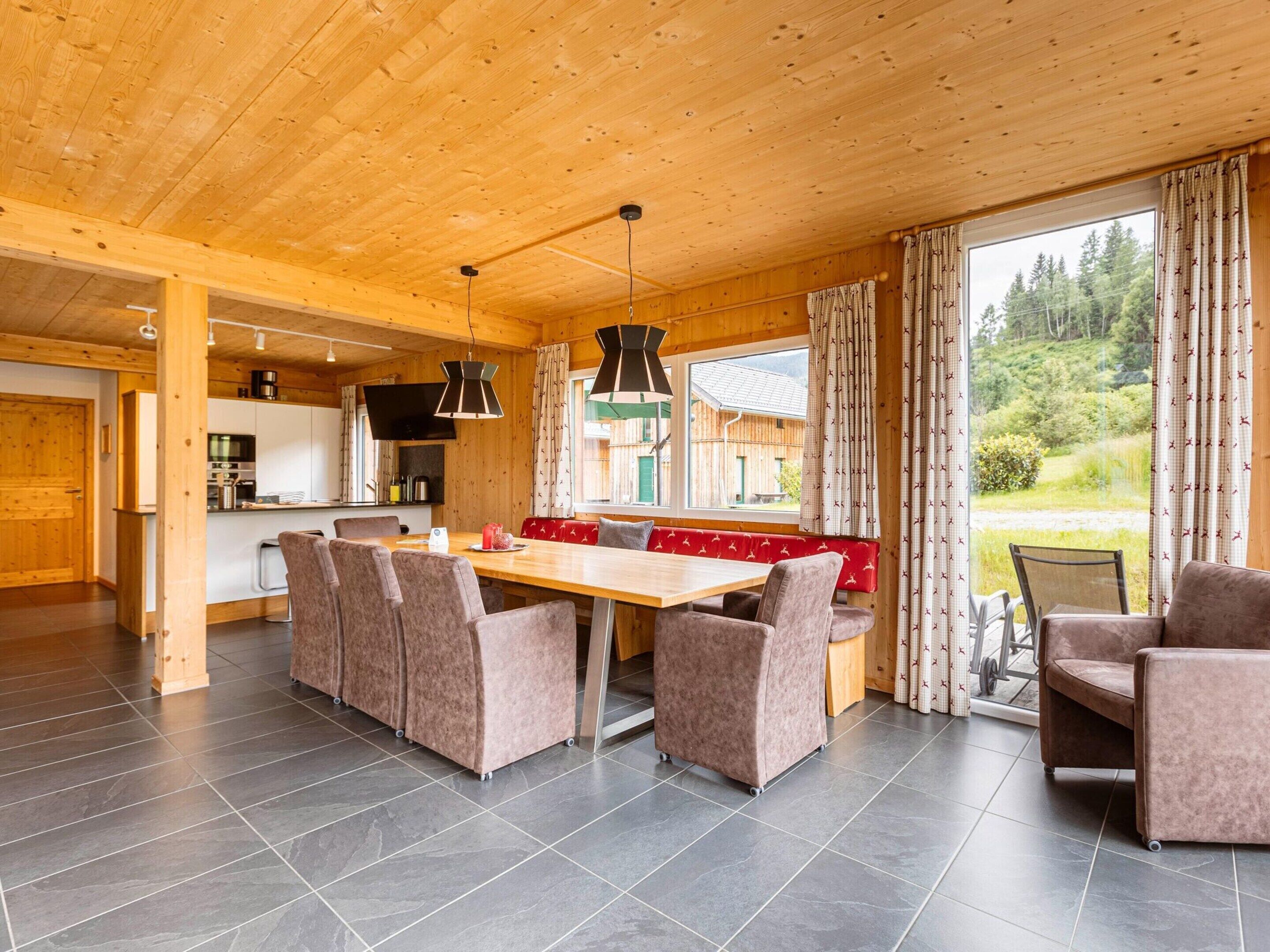 Interior moderno de una cabaña de troncos con comedor, cocina y grandes ventanales que ofrecen vistas del exterior.