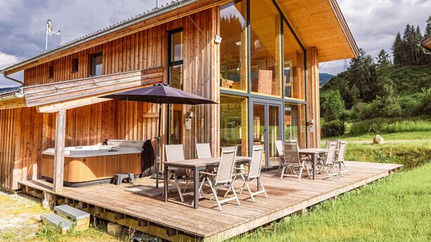 A wooden cabin with a deck, outdoor seating, and a sauna.