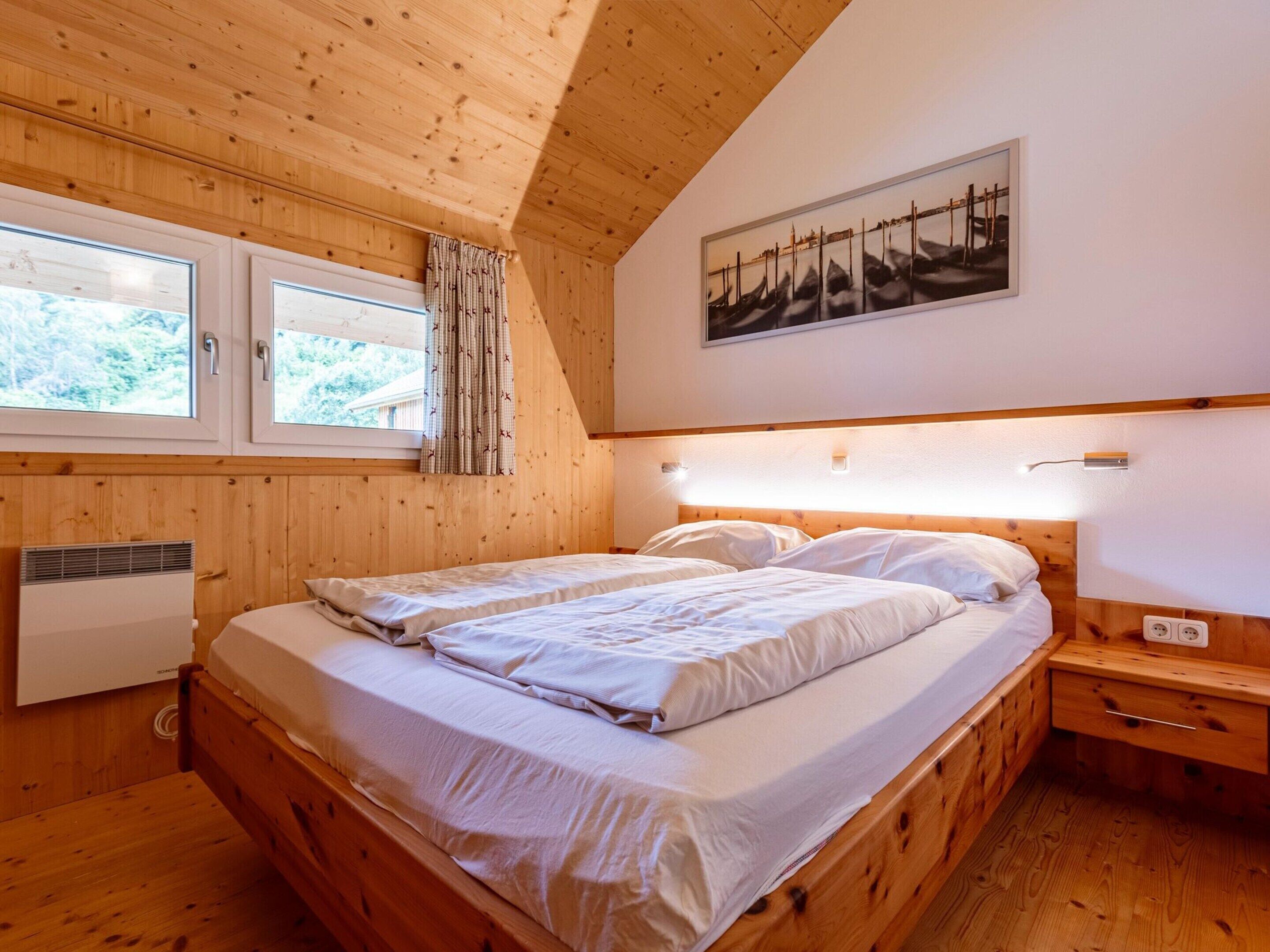 A wooden-paneled bedroom with two beds, a window with curtains, a radiator, and a painting on the wall.