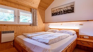 A wooden-paneled bedroom with two beds, a window with curtains, a radiator, and a painting on the wall.
