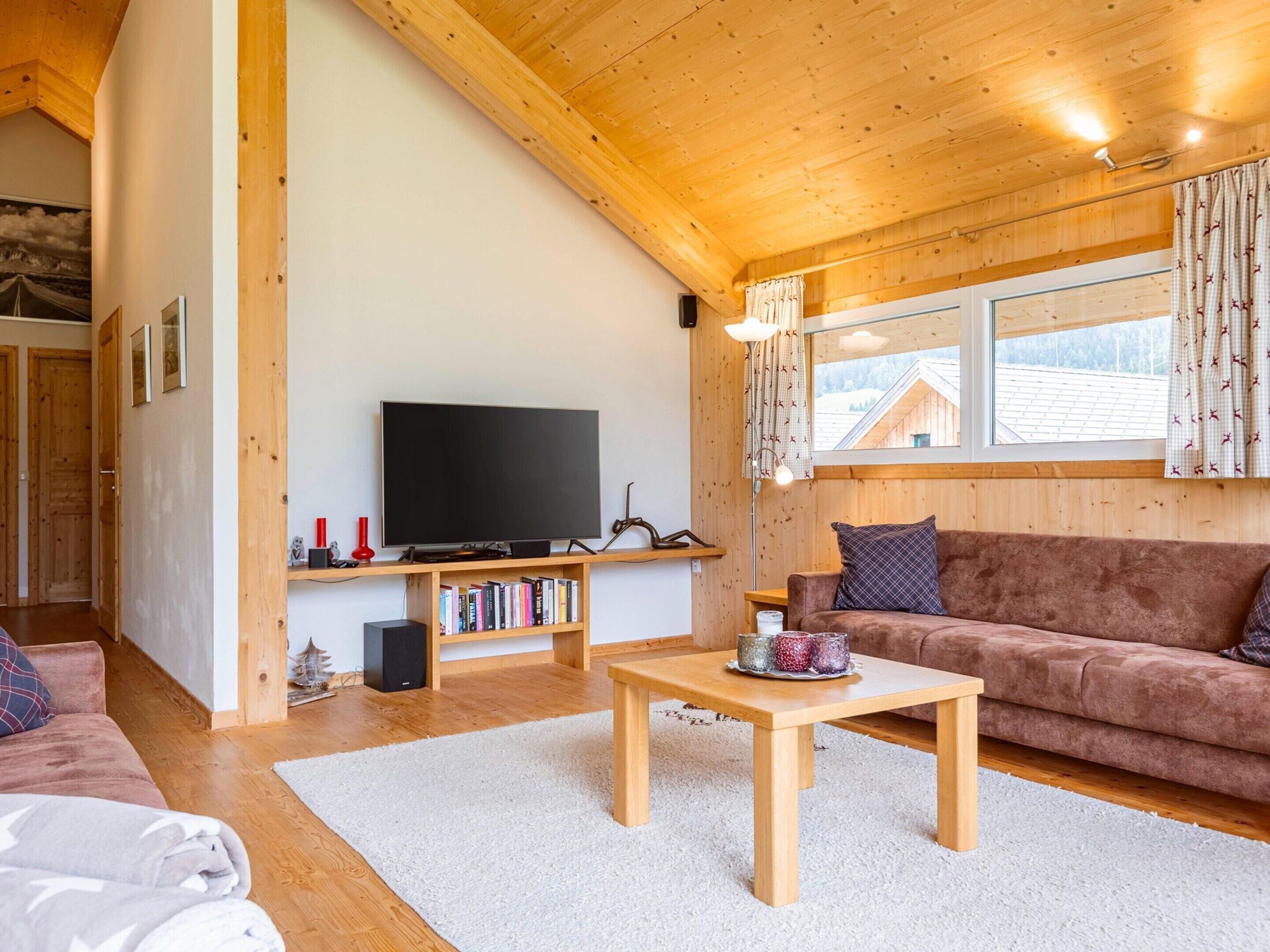 Una sala de estar acogedora con techo de madera, un televisor de pantalla plana, un sofá marrón, una mesa de centro y una estantería.