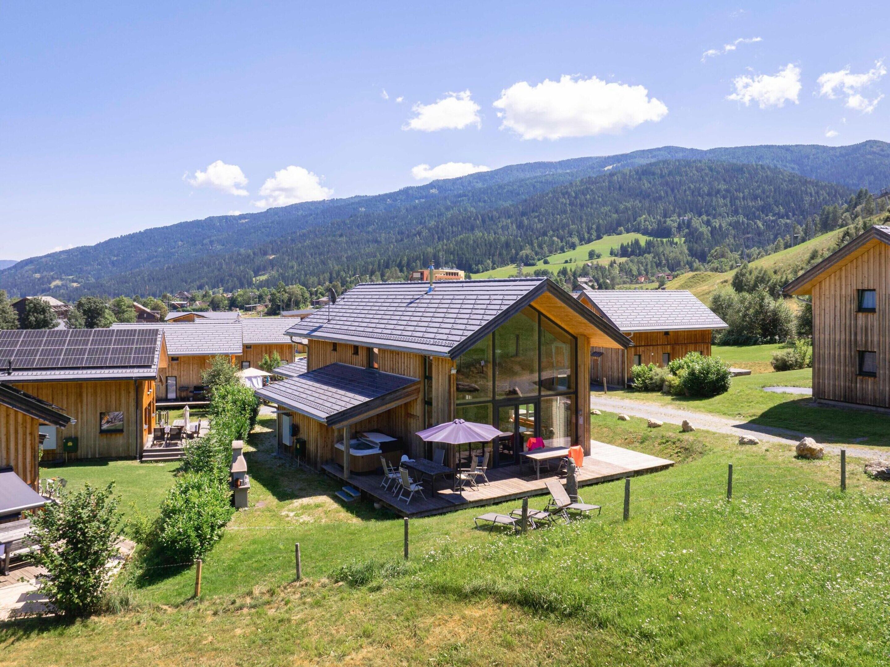 Eine Holzhütte mit Glasfassade, Solaranlagen und einer Terrasse mit Sitzgelegenheiten.