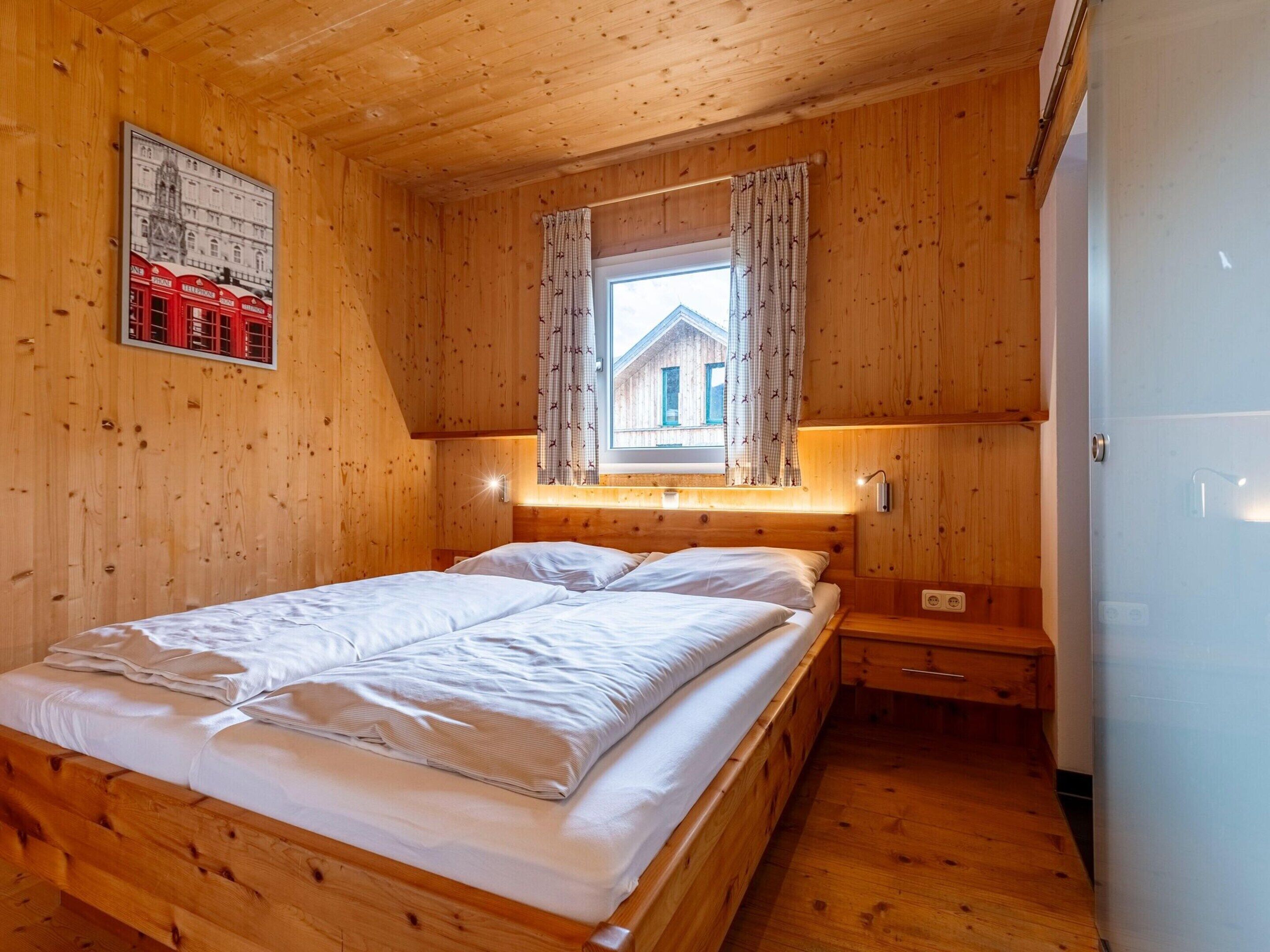 A wooden cabin bedroom with a bed, a nightstand, and a window with curtains.