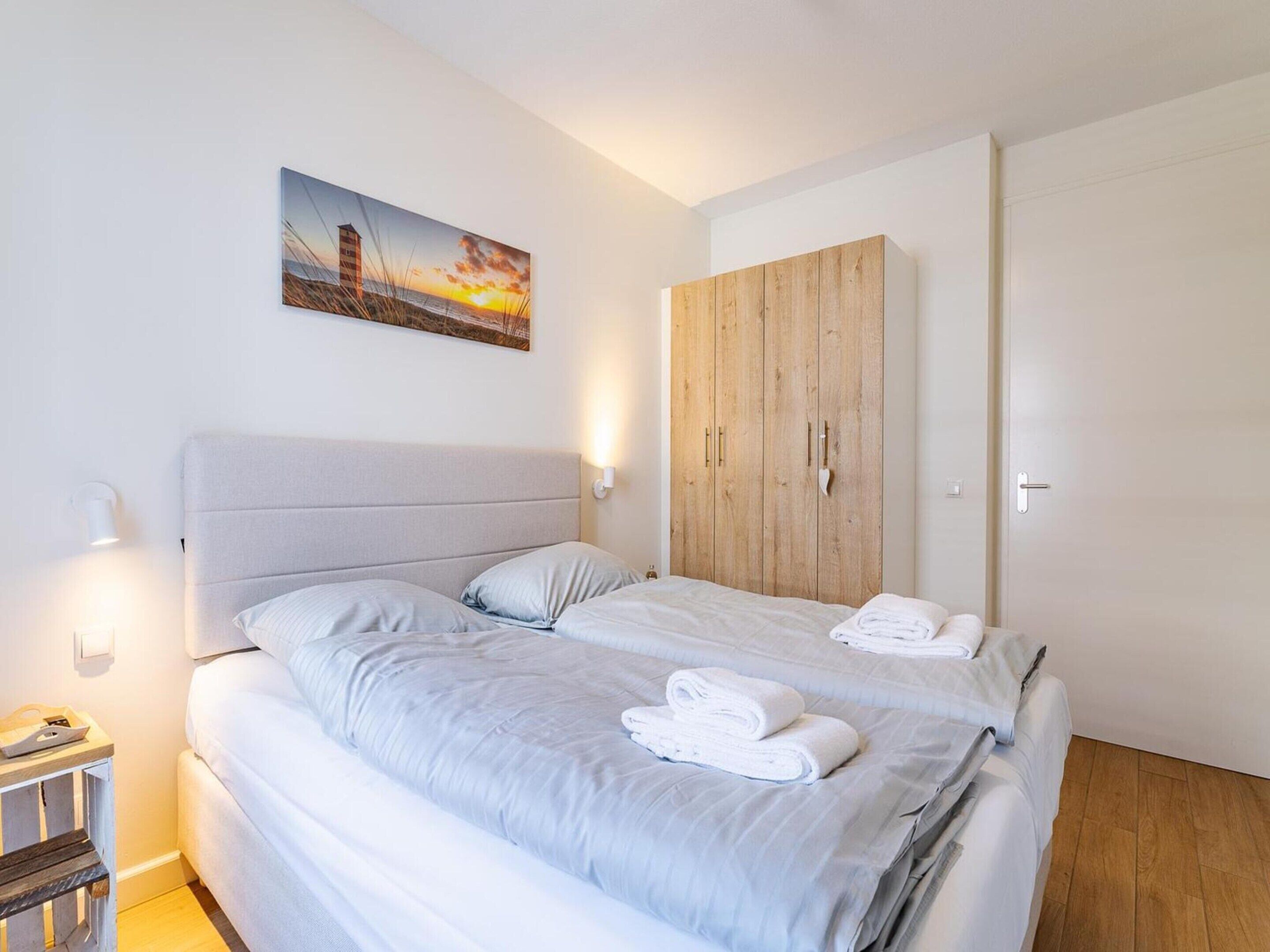 Un dormitorio con cama, armario de madera, un cuadro y una mesita de noche.