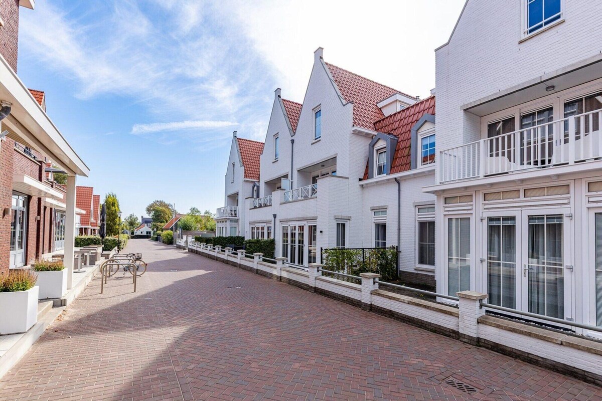 A street with white buildings, red roofs, and a paved walkway.