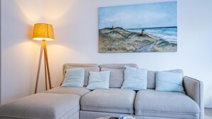Un soggiorno con un divano, una lampada da terra, un quadro raffigurante una spiaggia e un tavolino da caffè con oggetti decorativi.