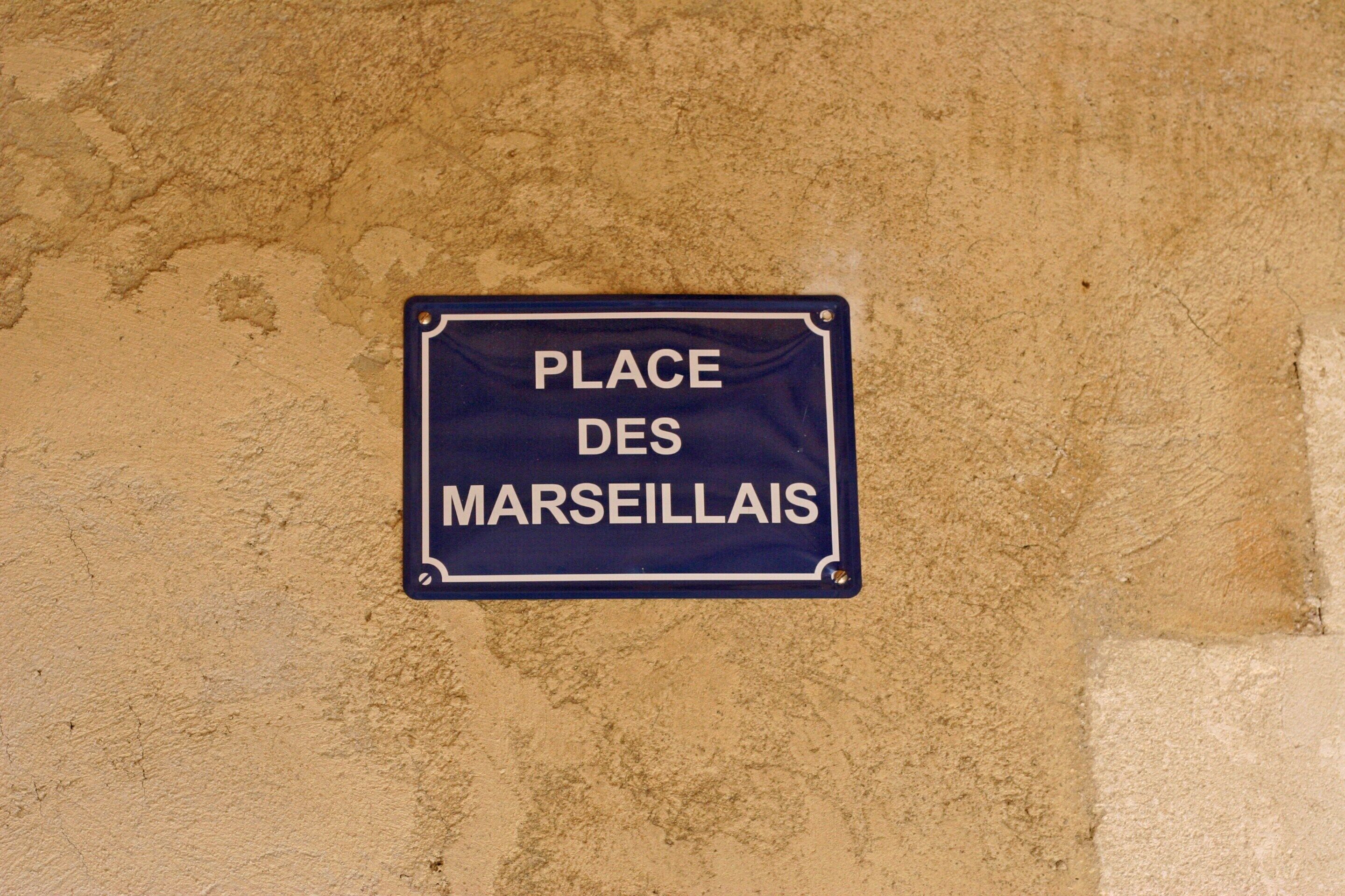 Een bord aan een structuurwand met de tekst 'PLACE DES MARSEILLAIS'.