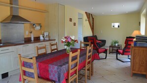 A dining area with a table set for four, a kitchen with a stainless steel range hood, and a staircase leading to another level. - Peaceful Stay Near Lake (Isigny-le-Buat)