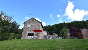 A stone building with a red umbrella, white chairs, and a fenced yard. - Peaceful Stay Near Lake (Isigny-le-Buat)