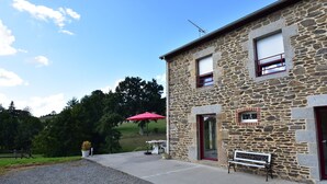 A stone building with a bench, a red umbrella, and a small table with a potted plant. - Peaceful Stay Near Lake (Isigny-le-Buat)