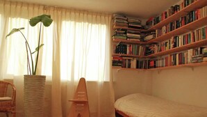 A room with a wooden bed, a bookshelf filled with books, a potted plant, a wicker chair, and a small stool. - Spacious Holiday Home With Garden (Egmond aan den Hoef)