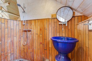 Une salle de bain aux murs lambrissés, avec un lavabo bleu, une pomme de douche et un miroir.