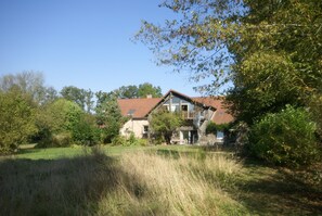 Une maison à deux étages, avec un toit rouge, entourée de verdure et d’une pelouse.
