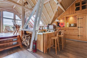 A rustic wooden interior with a high ceiling, a dining area with a bench, and a kitchen area with wooden cabinets and a brick wall. - Wellness & Adventure Escape (Niderviller)
