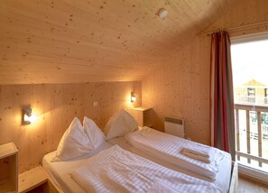 A wooden cabin room with a bed, a nightstand, a wall-mounted lamp, and a window with curtains. - Chalet With Infrared Sauna (Sankt Georgen am Kreischberg)