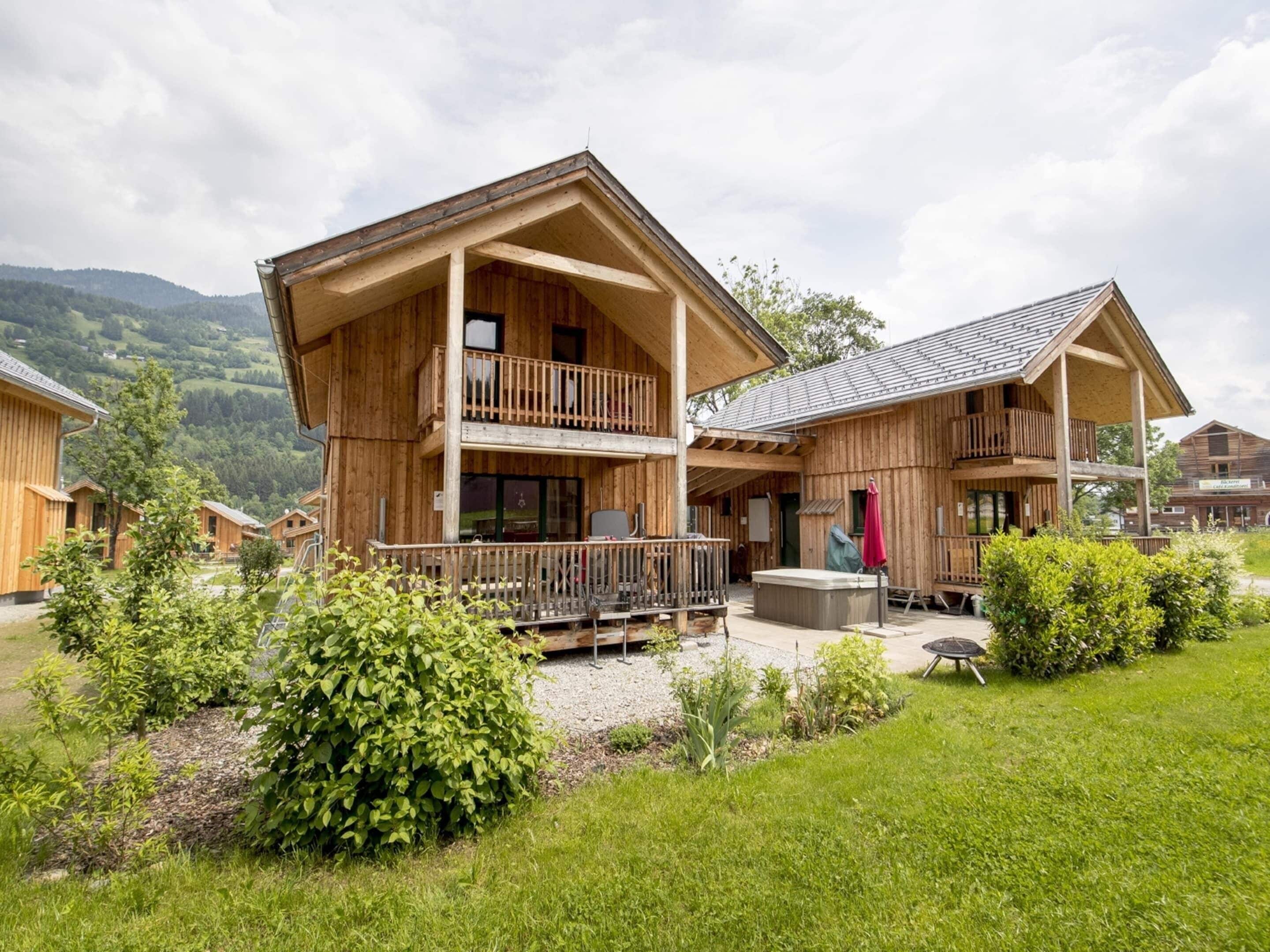 A wooden lodge with a balcony, a hot tub, and a view of the surrounding mountains.