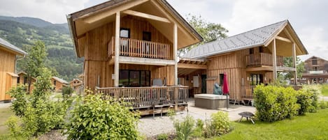A wooden lodge with a balcony, a hot tub, and a view of the surrounding mountains.
