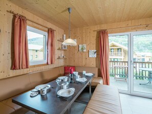 A wooden cabin with a dining area featuring a long table set for four, a sofa, and a view of the surrounding forest and buildings. - Chalet With Infrared Sauna (Sankt Georgen am Kreischberg)