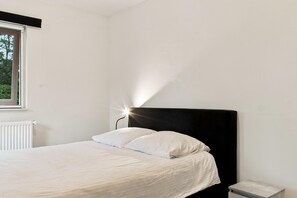 A single bed with a black headboard, white bedding, and a bedside table with a lamp. - Kempen Comfort With Sauna & Tub (Vessem)