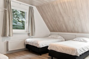 A bedroom with two beds, a window with curtains, a radiator, and a sloped ceiling. - Kempen Comfort With Sauna & Tub (Vessem)
