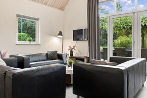 A modern living room with a sofa, armchair, and a flat-screen TV mounted on the wall. - Kempen Comfort With Sauna & Tub (Vessem)