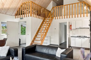 A modern interior with a wooden staircase, a kitchen area, and a seating area with leather sofas. - Kempen Comfort With Sauna & Tub (Vessem)