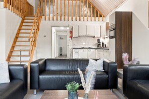 A modern living space with a black leather sofa, wooden staircase, and a kitchen area. - Kempen Comfort With Sauna & Tub (Vessem)