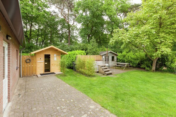 A brick building with a wooden door and a small wooden structure in the yard. - Kempen Comfort With Sauna & Tub (Vessem)