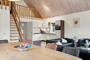 A modern kitchen with white cabinets, a wooden staircase, and a dining area with a table and leather seating. - Kempen Comfort With Sauna & Tub (Vessem)