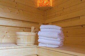 A wooden sauna room with a stack of towels and a wooden container with a handle. - Kempen Comfort With Sauna & Tub (Vessem)