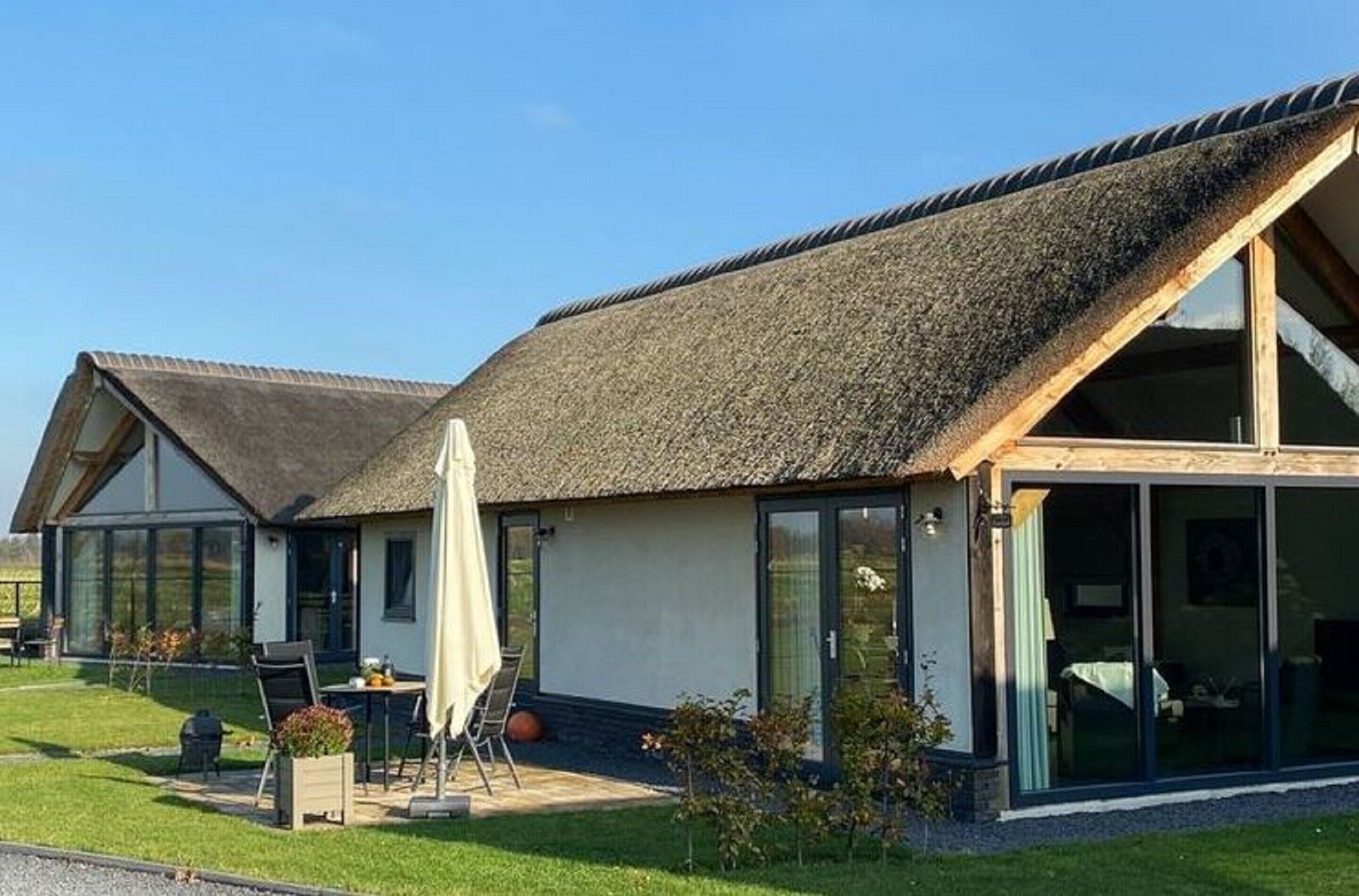 A modern house with a thatched roof, large glass windows, and a patio area with outdoor furniture.
