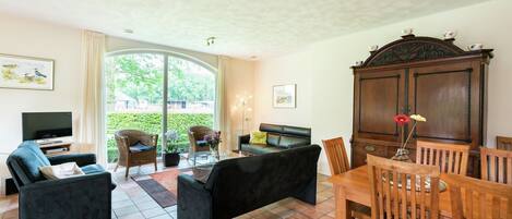 A living room with a sofa, a television, a dining table with chairs, and a cabinet.