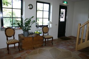 Quarto com escrivaninha de madeira, duas cadeiras, planta em vaso, luminária e vista pela janela.