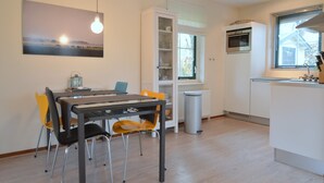 A modern kitchen with a built-in oven, a dining area with a table and chairs, and a window with blinds. - Holiday Home in Heeten Near Forest (Heeten)