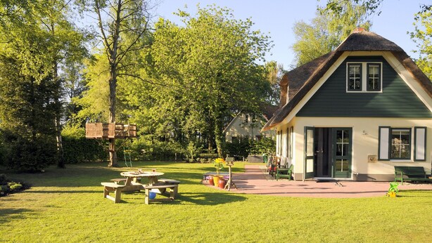 A traditional house with a thatched roof, surrounded by a well-maintained lawn and trees. - Holiday Home in Heeten Near Forest (Heeten)