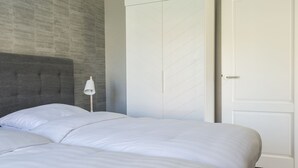 Camera da letto con due letti, una testiera grigia, una lampada da comodino bianca e un ampio armadio con motivi a diagonale.