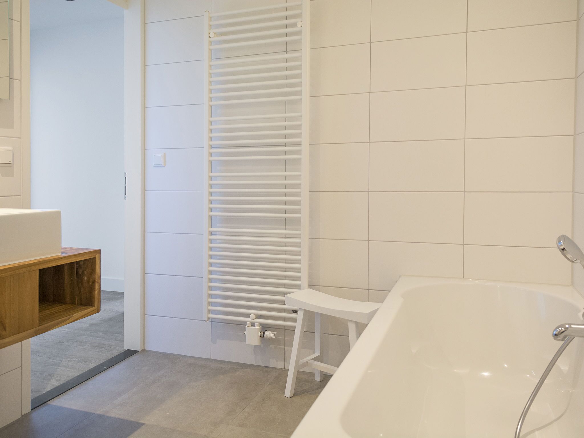A modern bathroom with a white bathtub, a wooden shelf, and a white towel rack.