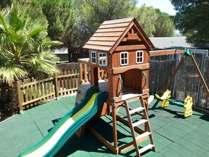 A wooden playhouse with a slide, a ladder, and a swing set. - 30m2 air-conditioned 2-bedroom chalet near Cap d'Agde beaches (Agde)