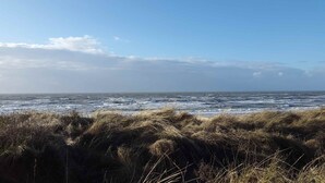 Een kustlandschap met ruwe zeegolven en grasduinen op de voorgrond.